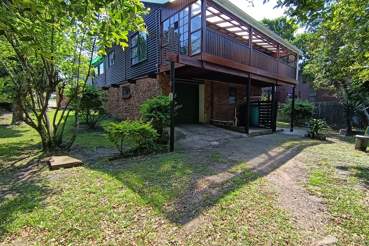 Rear view of a two-story house featuring a raised timber deck, brick lower level, and corrugated metal cladding with an integrated garage.