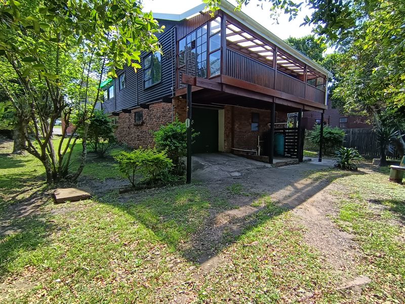 Rear view of a two-story house featuring a raised timber deck, brick lower level, and corrugated metal cladding with an integrated garage.
