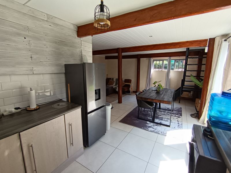 Open-plan living and dining area featuring exposed timber beams, a modern kitchen with subway tile backsplash, and a staircase leading to an upper level.