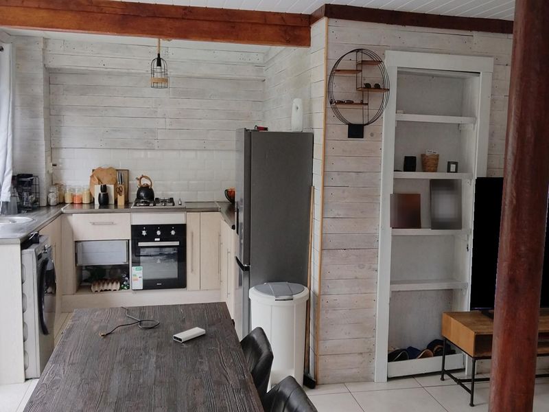 Open-plan kitchen and living area featuring white-washed timber wall cladding, exposed timber beams, built-in cabinetry, and tiled flooring.