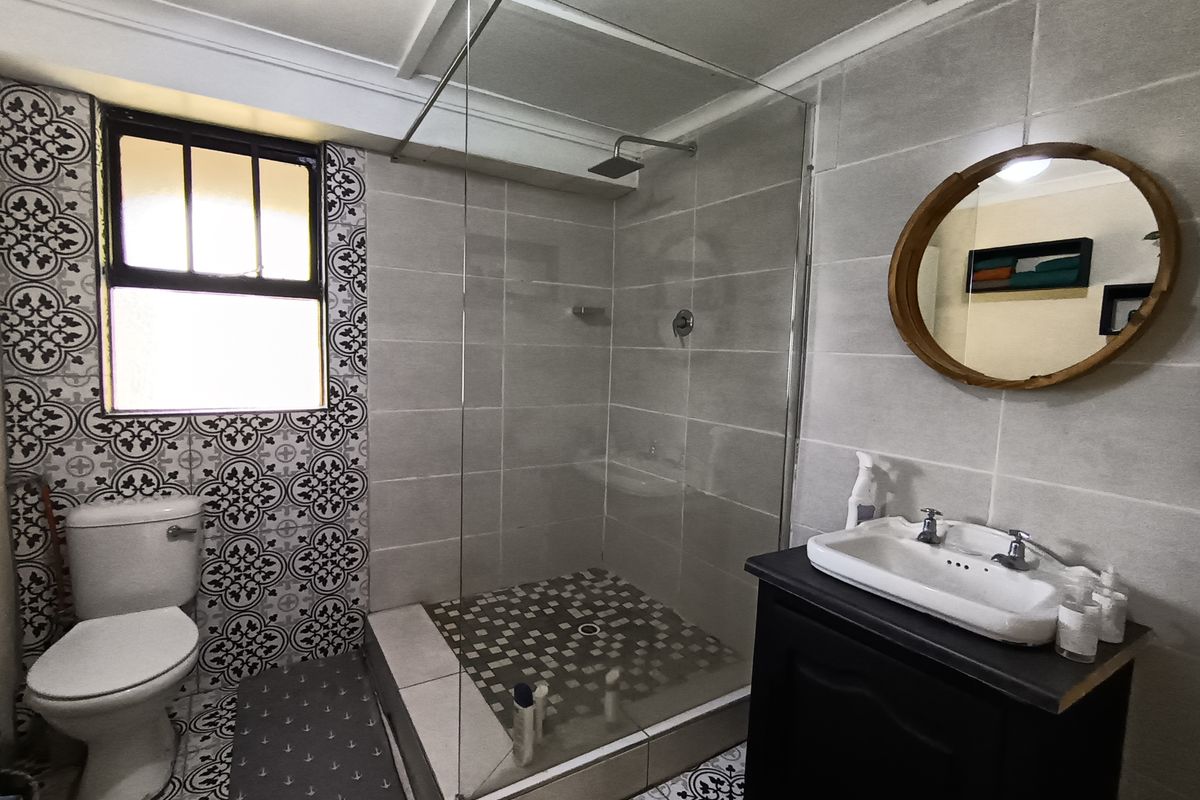 A modern bathroom featuring a walk-in shower with a glass screen, a vanity cabinet with a ceramic basin, and decorative patterned floor and wall tiles.