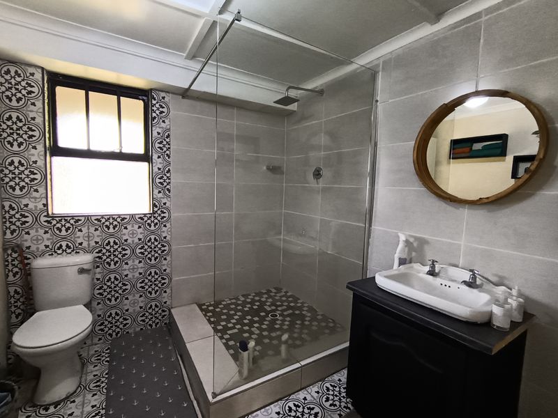 A modern bathroom featuring a walk-in shower with a glass screen, a vanity cabinet with a ceramic basin, and decorative patterned floor and wall tiles.