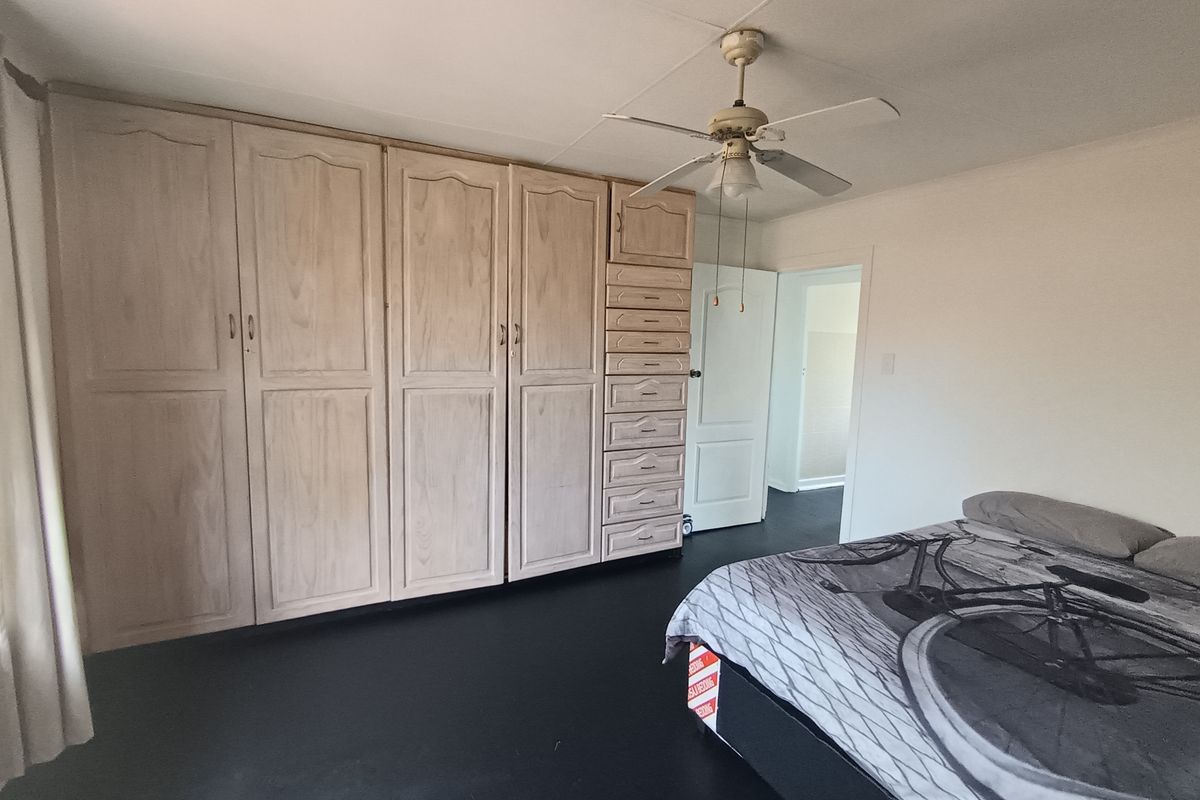 A bedroom featuring extensive built-in wooden cabinetry and a ceiling fan, with dark flooring and neutral wall finishes.