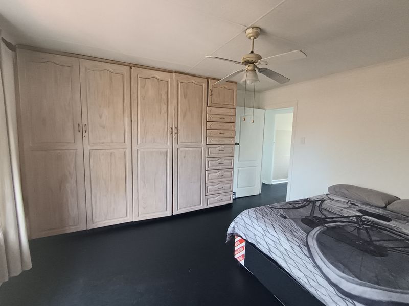 A bedroom featuring extensive built-in wooden cabinetry and a ceiling fan, with dark flooring and neutral wall finishes.