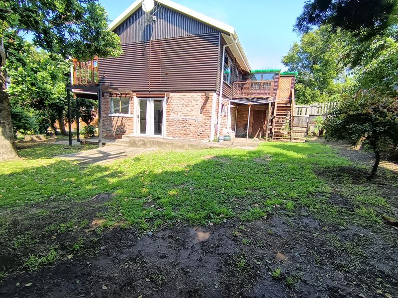 Rear view of a two-story house featuring a brick and timber facade, an elevated balcony with an external staircase, and a garden area.