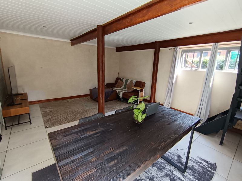 Open-plan living area featuring exposed timber beams, support columns, tiled flooring, and a tongue and groove ceiling with natural light.