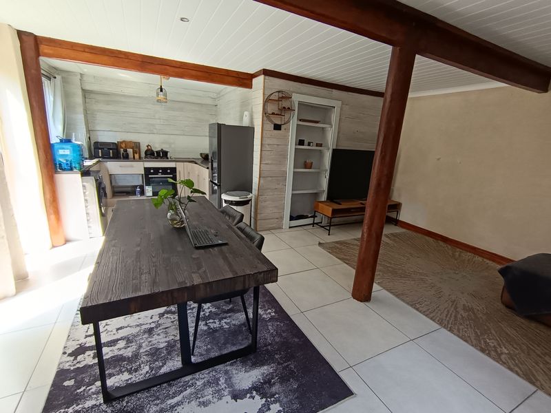 Open-plan living and kitchen area featuring exposed timber beams, tiled flooring, and built-in cabinetry, offering a rustic and functional layout.