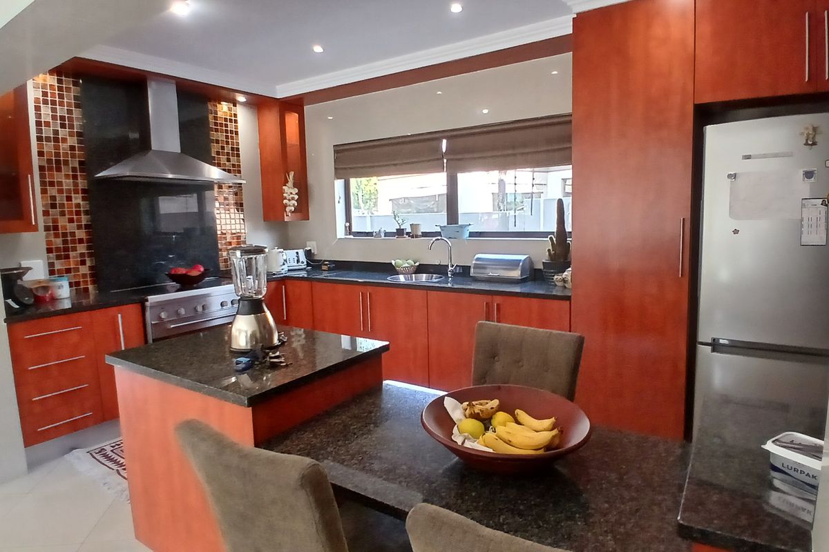 A well-maintained kitchen featuring warm-toned wooden cabinetry, dark granite countertops, a mosaic tile backsplash, and integrated stainless steel appliances.