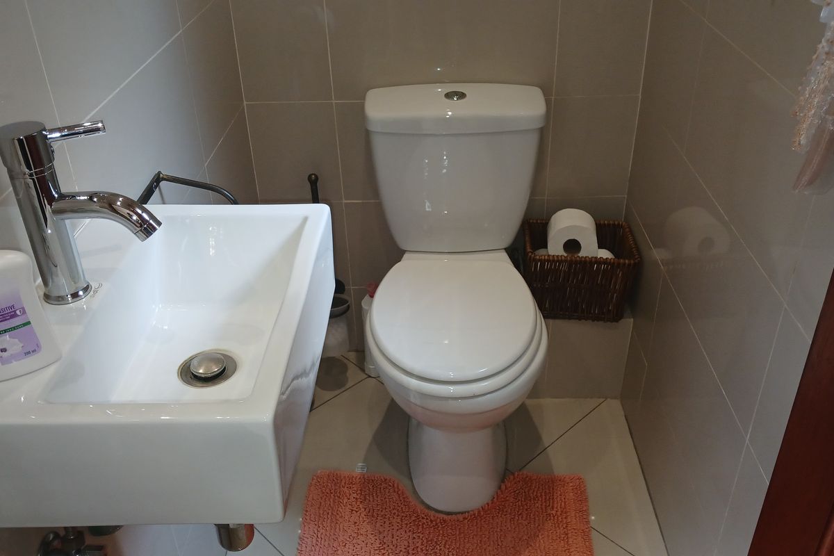 A compact guest bathroom featuring a modern wall-mounted basin with chrome mixer tap and a standard close-coupled toilet, finished with neutral ceramic tiling.