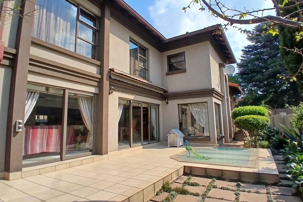 Rear view of the double-story house featuring a tiled patio area, large sliding glass doors, and a landscaped garden with paved pathways.