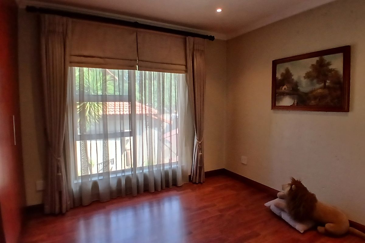 A bright and spacious bedroom featuring warm laminate flooring, built-in wardrobe storage, and large windows with elegant curtain treatments.