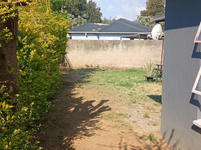 A rear garden area featuring a perimeter wall, established hedge, and exterior wall with security-fitted top-hung windows.