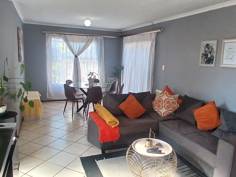 Open-plan living and dining area featuring tiled flooring, neutral grey walls, and sliding glass doors providing natural light.