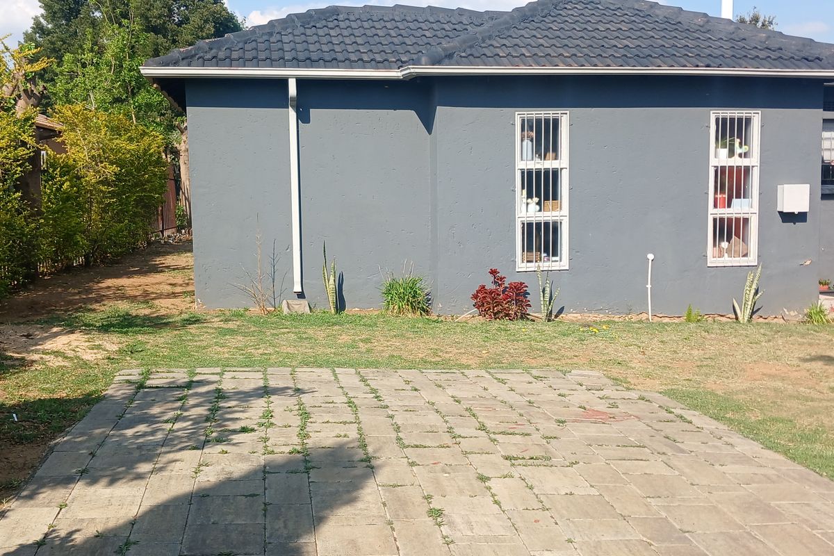 Rear view of the property featuring a paved area, lawn, and a grey exterior wall with security-barred windows.