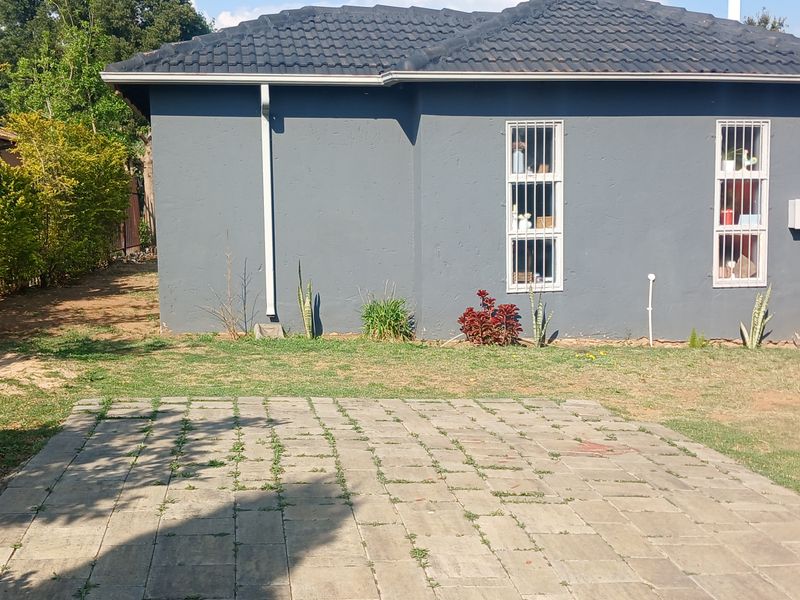 Rear view of the property featuring a paved area, lawn, and a grey exterior wall with security-barred windows.