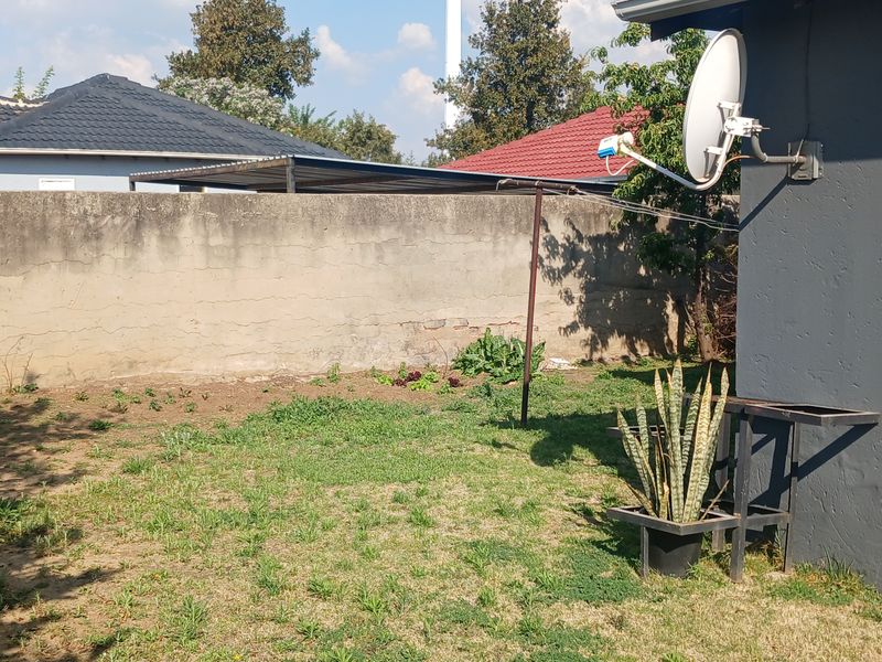A rear garden area featuring a boundary wall, a satellite dish, and a washing line, adjacent to the exterior wall of the house.