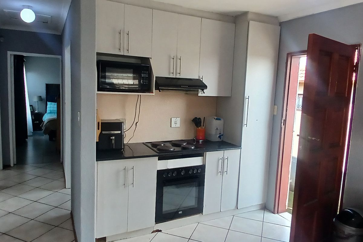 Compact kitchen featuring white cabinetry, black countertops, built-in oven, hob, and extractor fan, with tiled flooring and direct access to an exterior door.