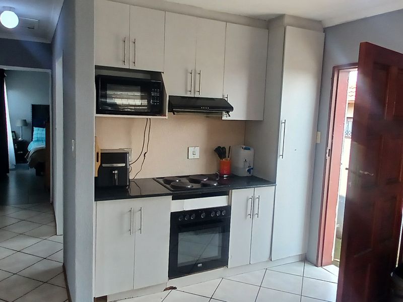 Compact kitchen featuring white cabinetry, black countertops, built-in oven, hob, and extractor fan, with tiled flooring and direct access to an exterior door.