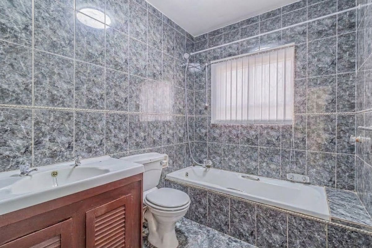 A functional bathroom featuring full-height marble-effect wall tiling, a built-in vanity, a standard bathtub with shower mixer, and a toilet.