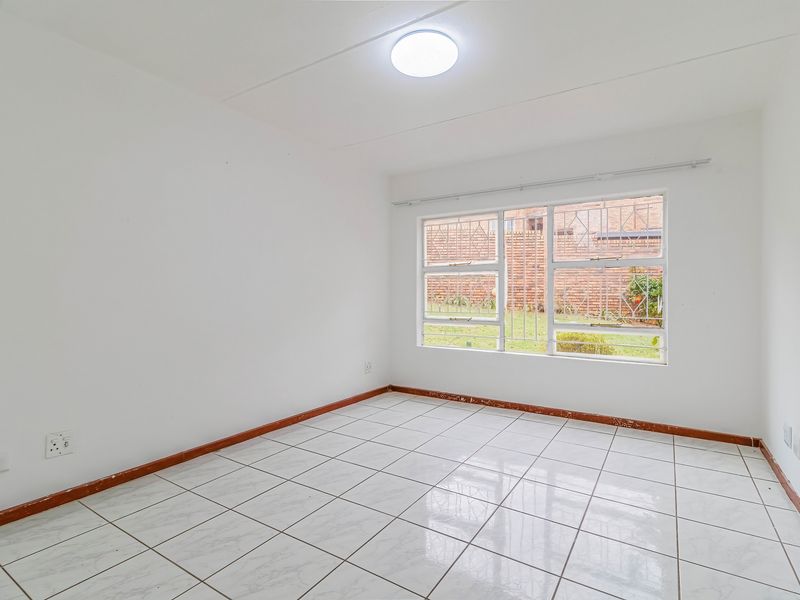 An empty bedroom featuring white walls, tiled flooring, and a window with security bars, providing a blank canvas for personalization.