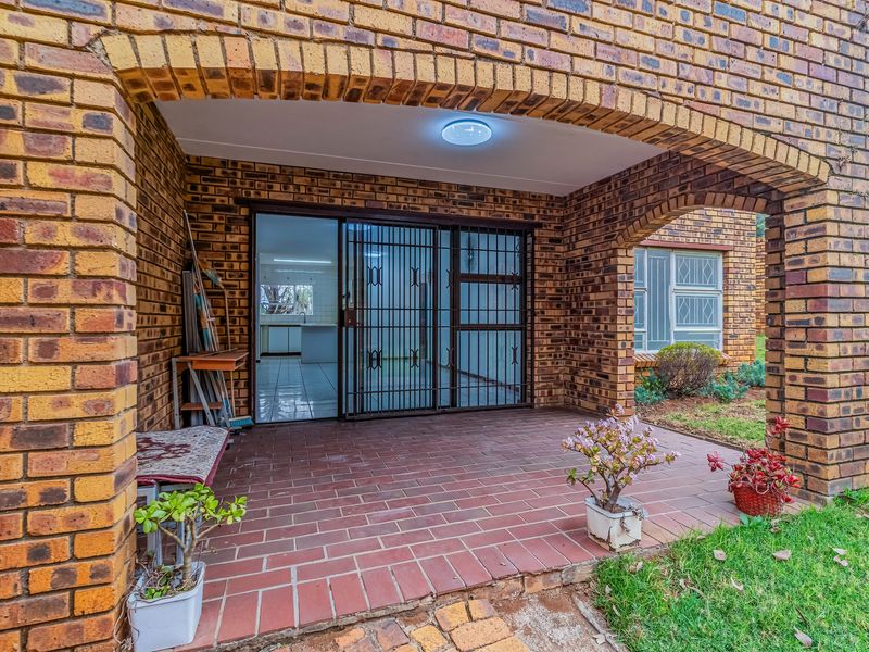 A covered brick patio area featuring an arched entrance, tiled flooring, and a secure sliding glass door leading into the interior living space.