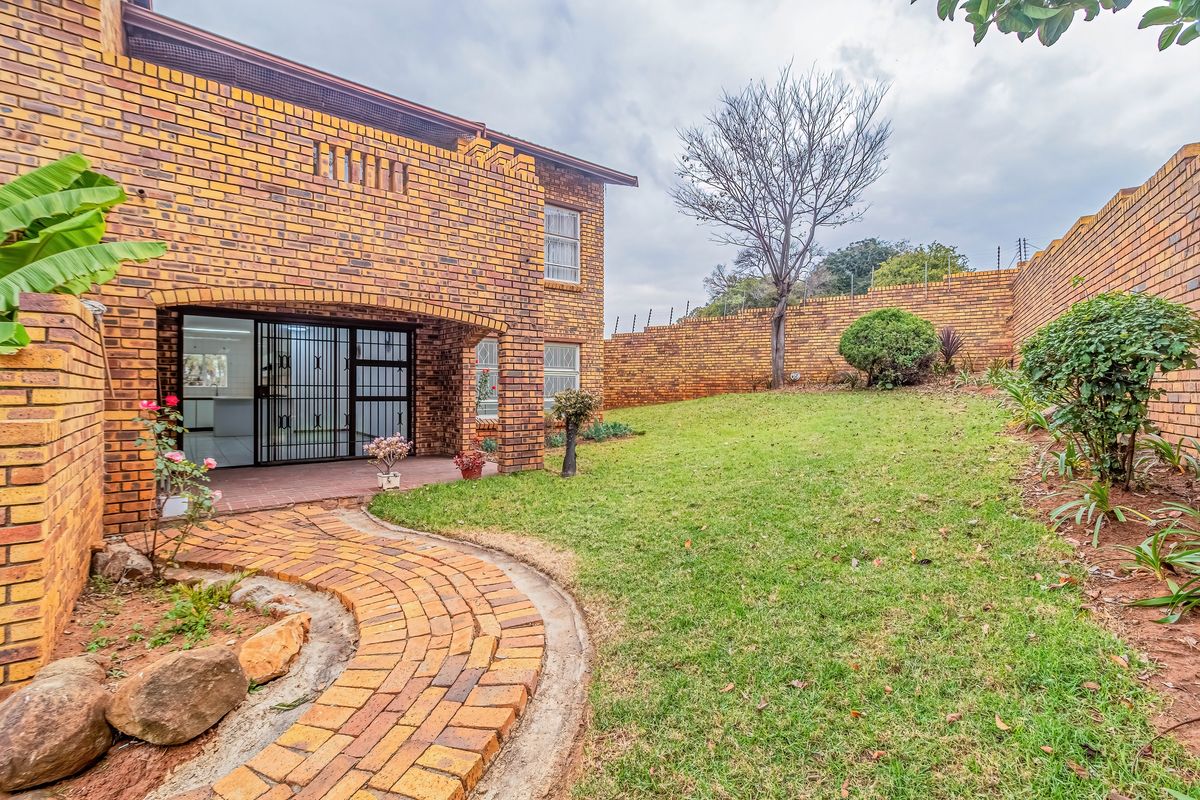 Rear view of the townhouse featuring a face-brick facade, a covered patio, a brick-paved pathway, and a private garden enclosed by a high perimeter wall.