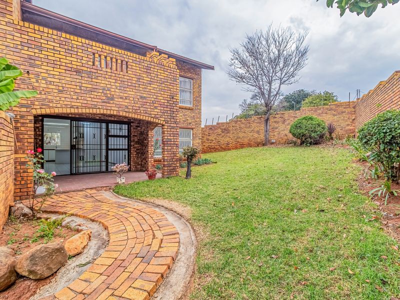 Rear view of the townhouse featuring a face-brick facade, a covered patio, a brick-paved pathway, and a private garden enclosed by a high perimeter wall.