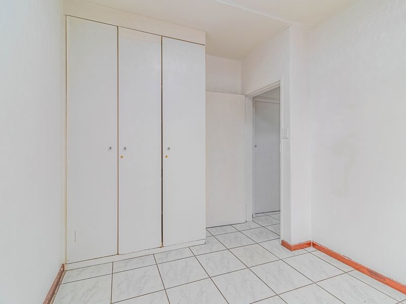 A vacant hallway featuring built-in storage cupboards and tiled flooring, requiring minor cosmetic updates to skirting and paintwork.