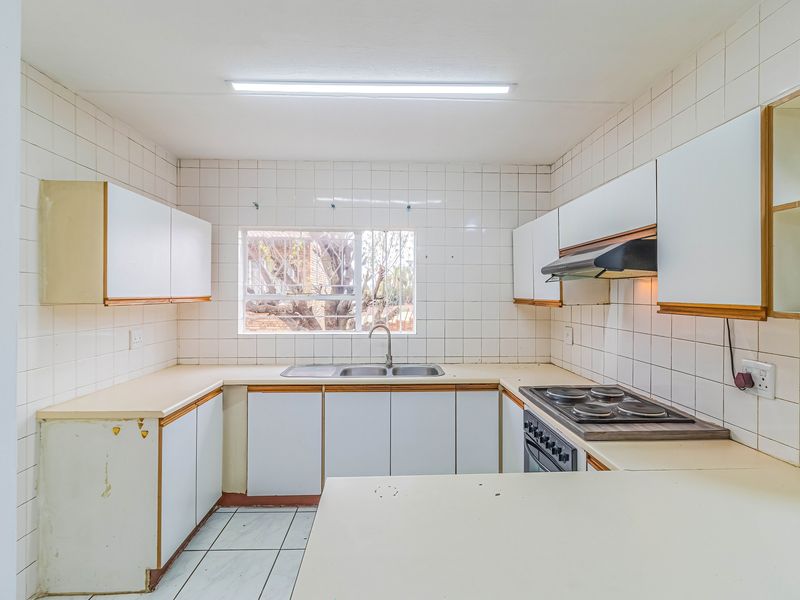 A functional kitchen featuring built-in cabinetry, laminate countertops, a double basin sink, and integrated electric cooking appliances with tiled finishes throughout.
