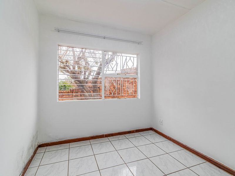An empty bedroom featuring tiled flooring, security bars on the window, and visible signs of damp on the lower wall section.