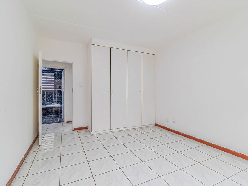 An empty bedroom featuring white built-in wardrobes, ceramic tiled flooring, and direct access to an en-suite bathroom.