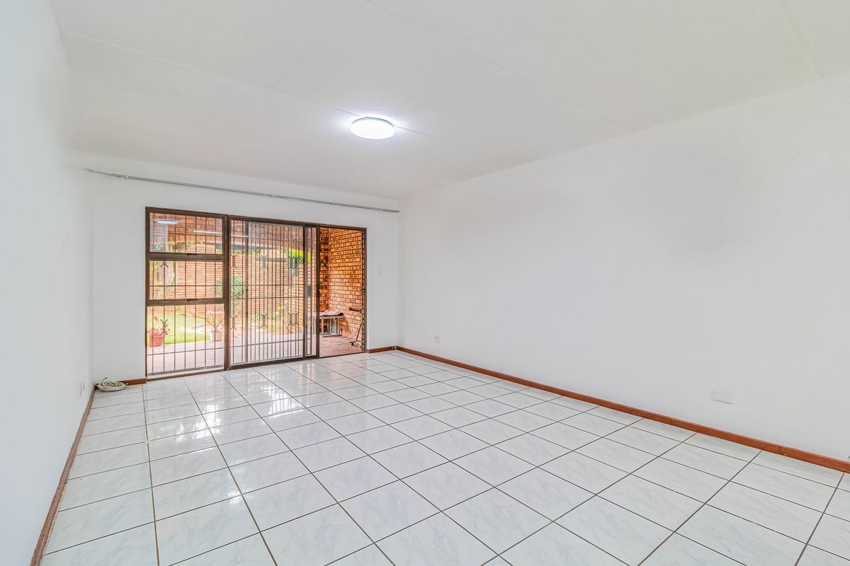 A bright, empty living room featuring white tiled flooring and a sliding glass door with a security gate leading to the outdoor area.