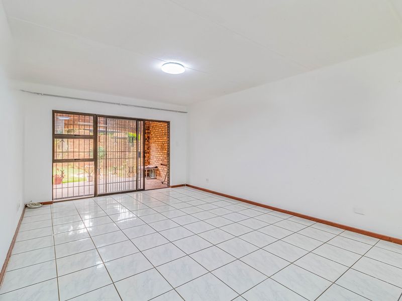 A bright, empty living room featuring white tiled flooring and a sliding glass door with a security gate leading to the outdoor area.