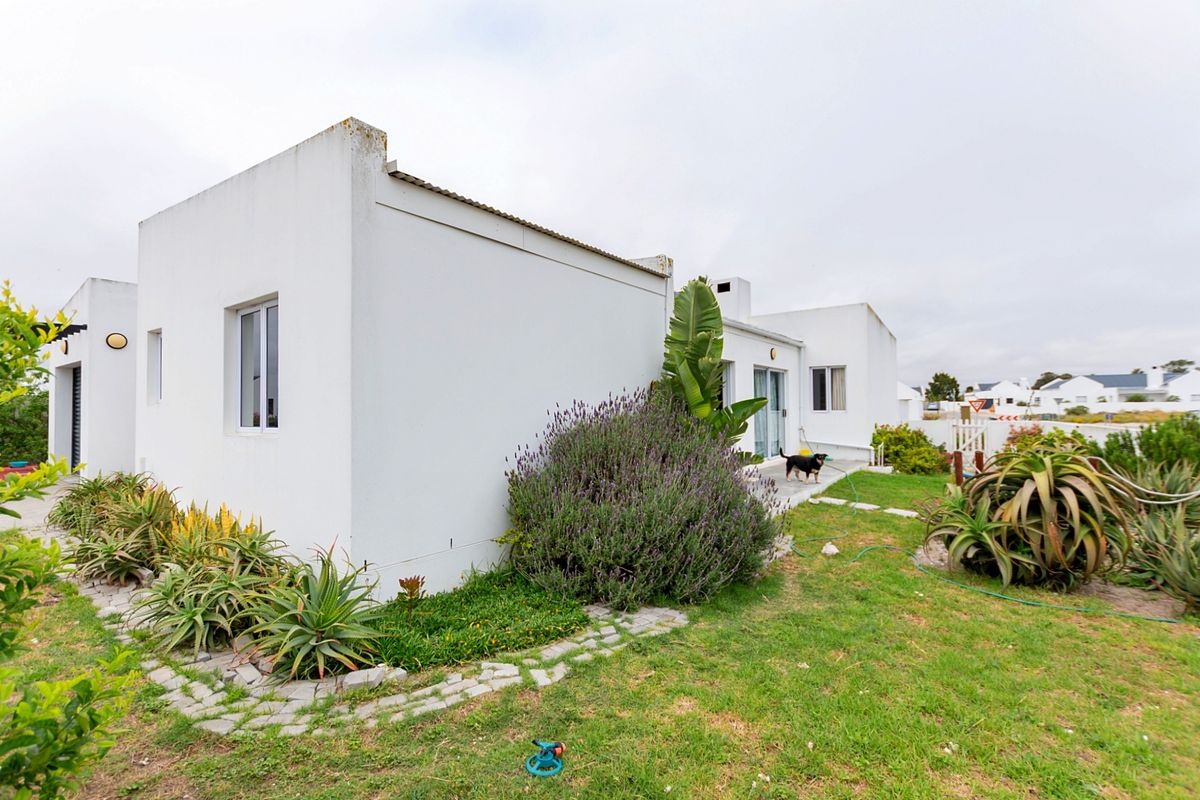 Rear view of a white-walled residential property featuring a landscaped garden, paved pathways, and sliding glass door access.