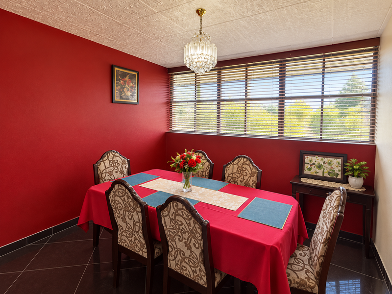 A dining room featuring dark tiled flooring, a textured ceiling, a crystal chandelier, and large windows with venetian blinds.