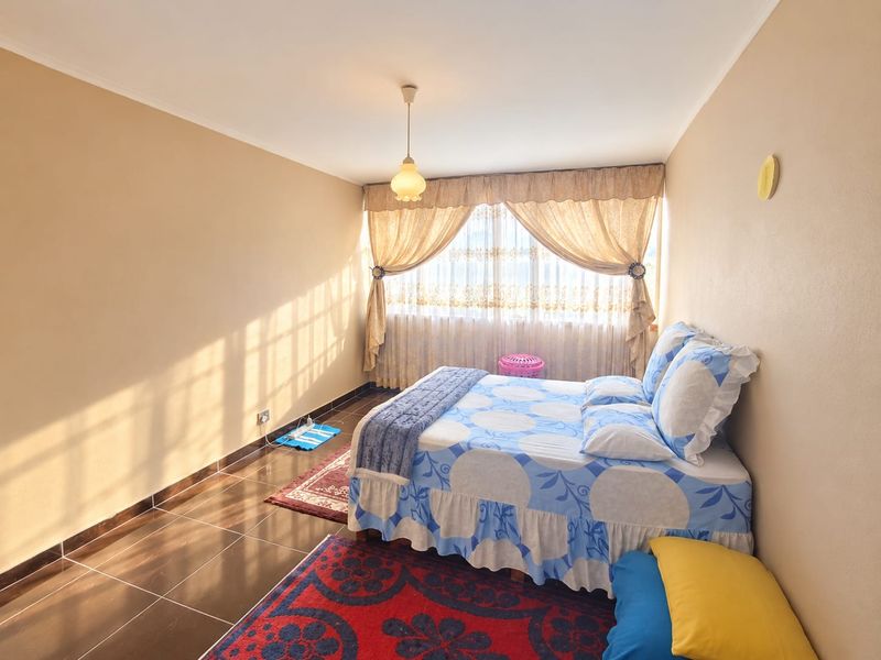 A bedroom featuring tiled flooring, neutral wall finishes, and natural light through window curtains.
