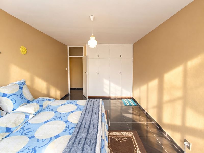 A bedroom featuring built-in cupboards, dark tiled flooring, and a pendant light fixture, with warm natural light entering from the side.