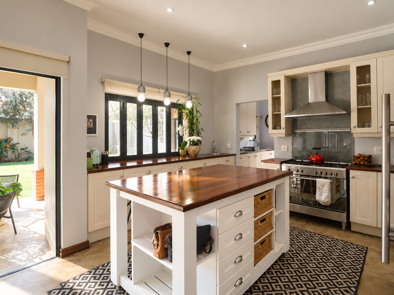 A bright, well-maintained kitchen featuring a central wooden island, gas stove with extractor, and direct access to an outdoor patio area.