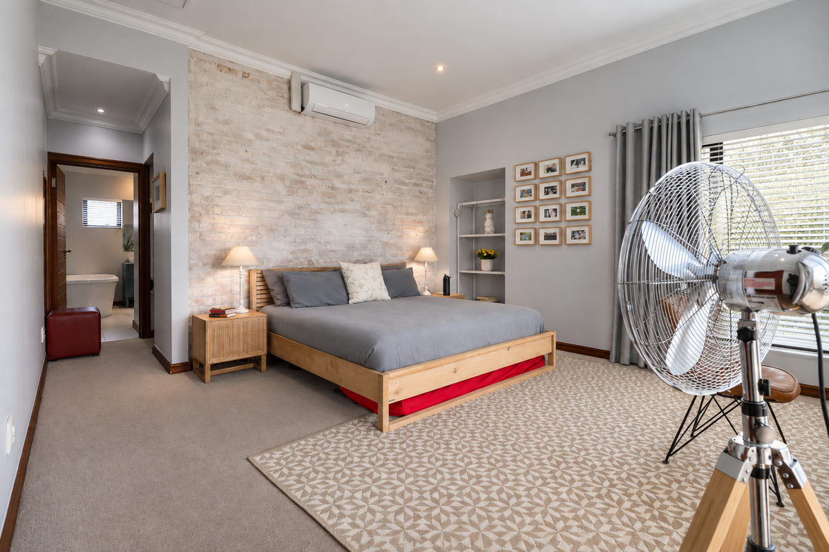 Spacious bedroom featuring an exposed brick accent wall, split-system air conditioning, and an adjoining ensuite bathroom.