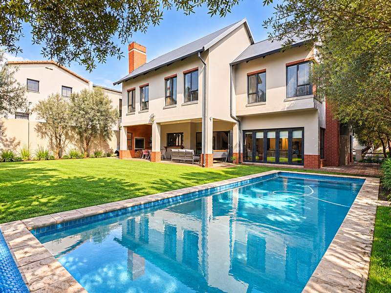 A well-maintained rear exterior view featuring a landscaped garden, a swimming pool with stone coping, and a covered patio area.