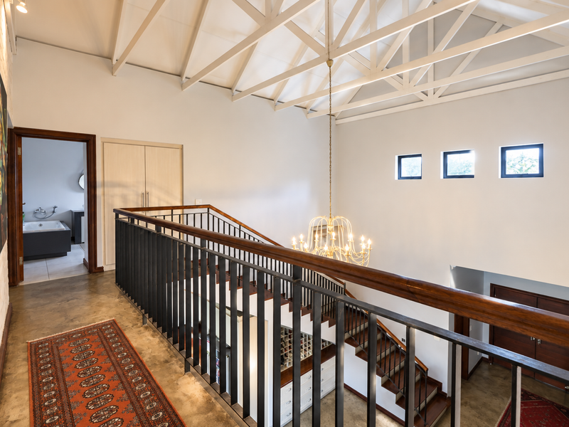Spacious upper-level landing featuring exposed white vaulted roof trusses, a modern metal balustrade with a wooden handrail, and access to an en-suite bathroom.