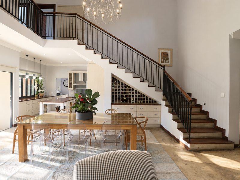 Spacious open-plan living and dining area featuring a grand staircase with wrought iron balustrade, built-in wine storage, and a modern kitchen with island.