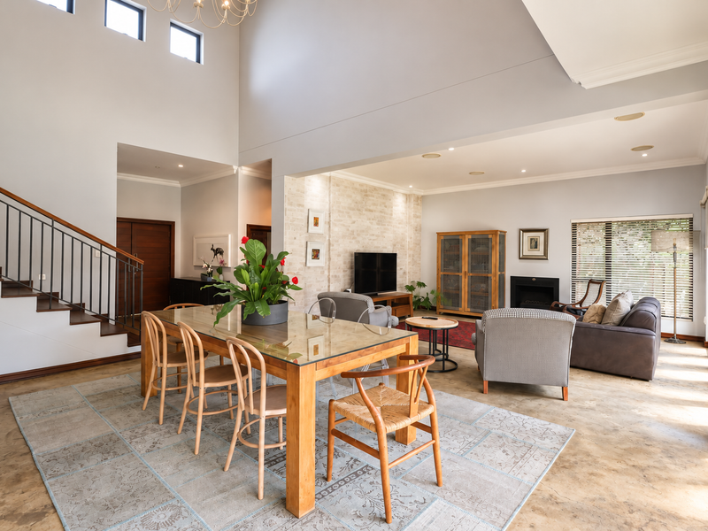 Spacious open-plan living and dining area featuring high vaulted ceilings, a striking exposed brick fireplace wall, and a modern staircase with metal balustrades.