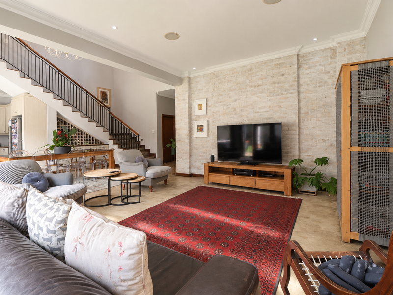 Spacious open-plan living area featuring a striking exposed brick wall, polished concrete floors, and a modern staircase with an integrated wine rack.