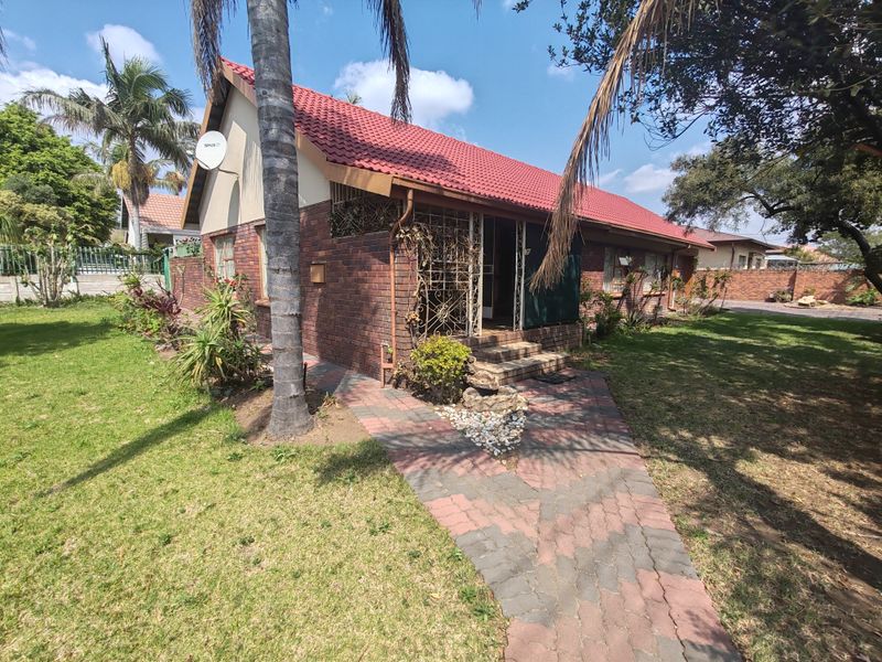 Front view of a single-story brick house featuring a tiled roof, paved walkway, and established garden surroundings.