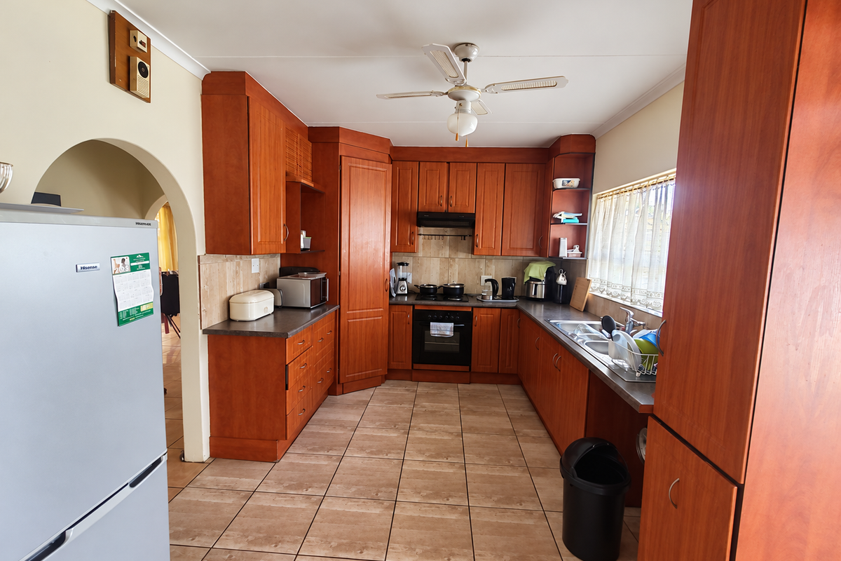 A functional kitchen featuring warm-toned wooden cabinetry, tiled flooring, built-in oven with extractor fan, and a double sink with ample counter space.