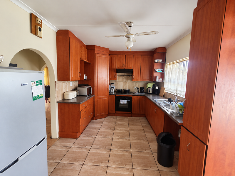 A functional kitchen featuring warm-toned wooden cabinetry, tiled flooring, built-in oven with extractor fan, and a double sink with ample counter space.