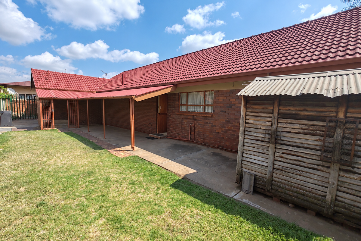 Rear view of the property featuring a brick facade, tiled roof, and a covered patio area overlooking the garden.