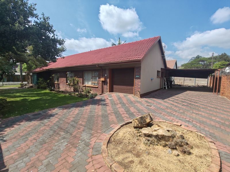 Front exterior view of a single-story brick house featuring a paved driveway, attached garage, and a covered carport area.