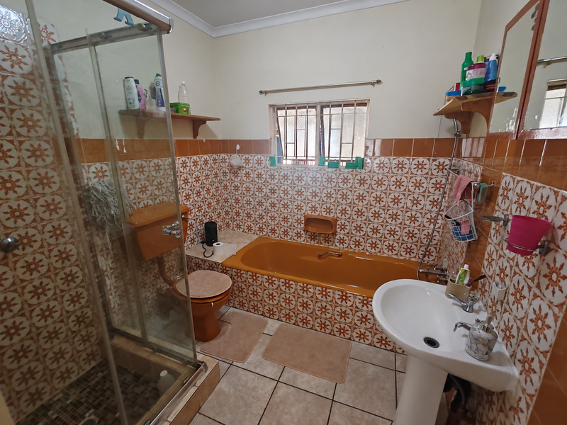 A dated bathroom featuring a colored bathtub, pedestal sink, shower enclosure, and patterned wall tiles throughout.